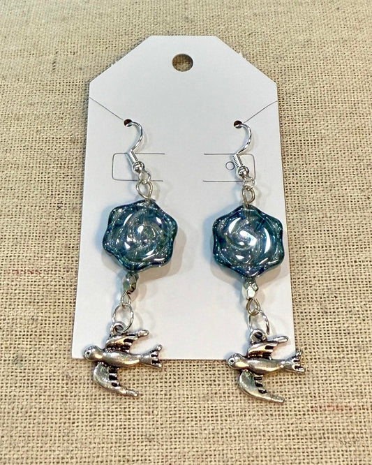 Pair of earrings with blue hexagonal beads and silver swallow charms on a white card.
